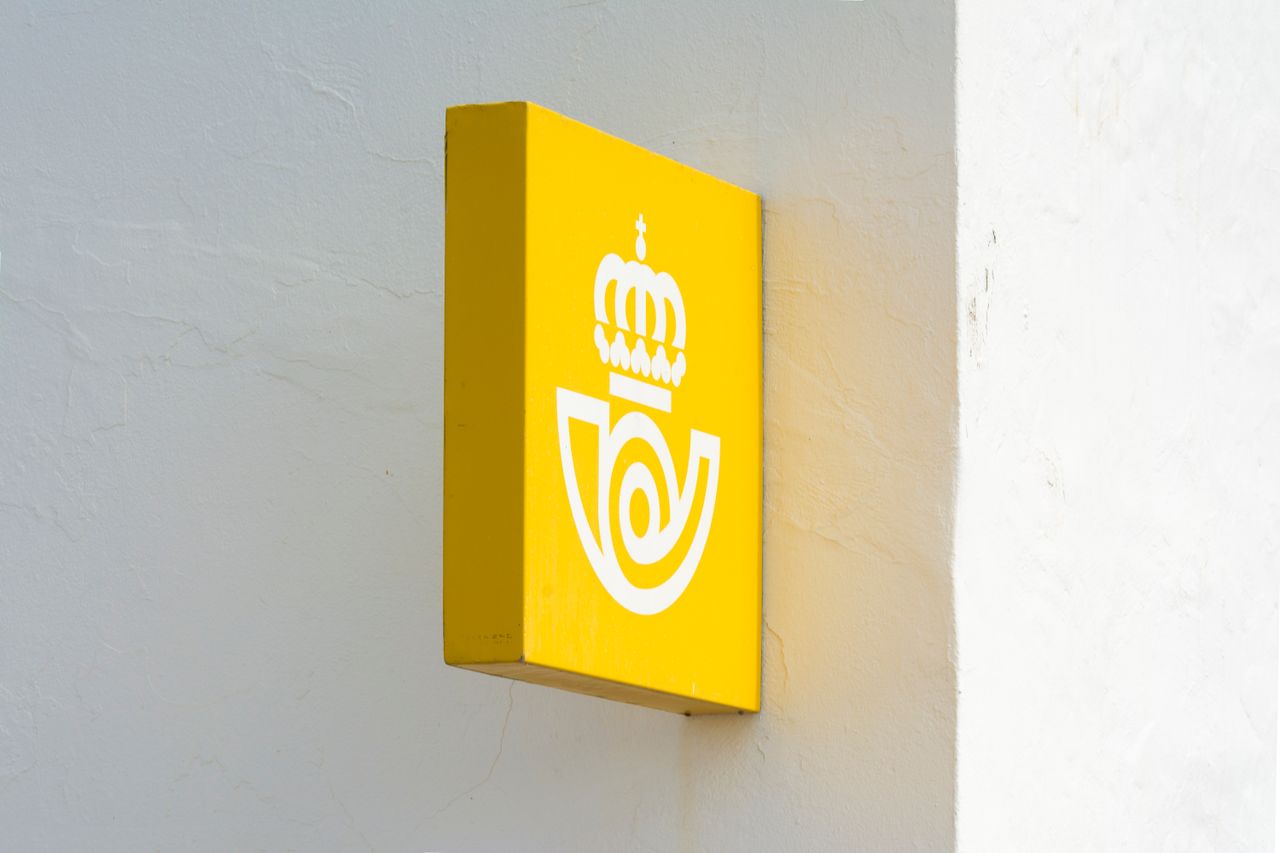 A striking yellow sign featuring a crown logo attached to a white wall, with clear, minimalistic design.